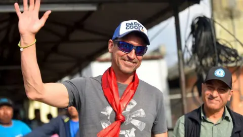 Kenton Cool, in a trucker cap and grey T-shirt, waves upon arriving at the airport in Kathmandu on 19 May, 2023, after he reached the top of Everest for the 17th time