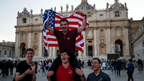 Men applaud while holding an American flag outside the Vatican