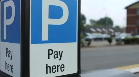 A blue parking sign on a machine in a car park.