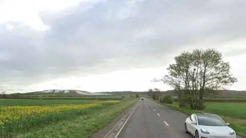 A country road flanked by large fields and trees.