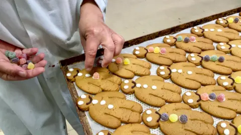 A tray of gingerbread men being decorated with icing and jelly tot sweets.
