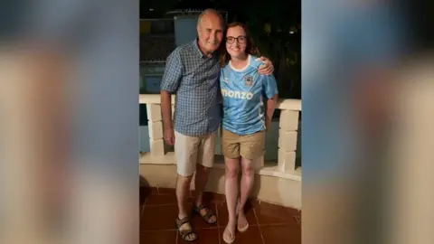 Emma Arnsho Emma Ernsho é uma risada com o pai. Ele usava uma camisa de Coventry City e shorts cáqui enquanto estava ao lado de seu pai, que estava sorrindo, vestindo uma camisa verificada com azul claro e shorts creme.