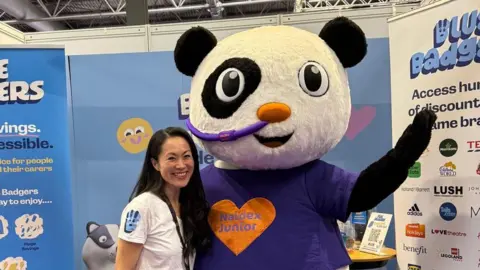 Family A woman stands with a panda mascot and a convention. 