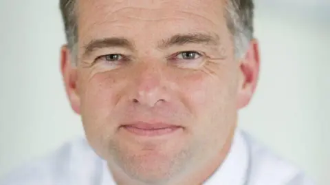 Nick Page smiles at the camera. He has grey hair and wears a white shirt.