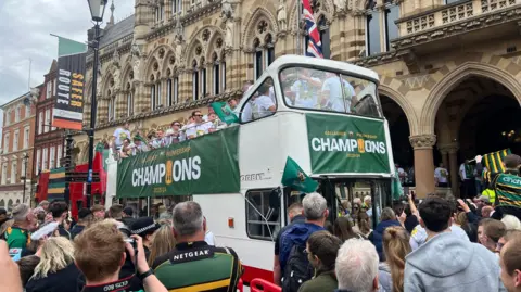 Northampton Saints players travel through the town centre in an open-top bus.