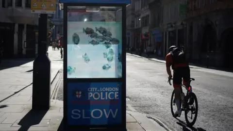 PA Media Police sentry box of a shoal of fish artwork on it on the glass windows of the cubicle. At the side, a cyclist rides by.