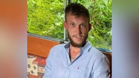 A man with a blue shirt and short hair and a beard