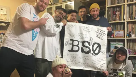 Naoki Iijima Image of Bristol artists and Mr Iijima holding flag reading BS0.