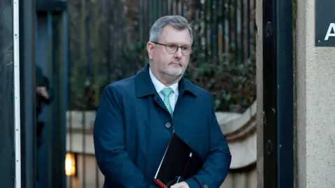 PA Media Sir Jeffrey Donaldson, pictured with short grey hair wearing glasses, a white shirt, blue tie and navy jacket. He is holding a notepad.