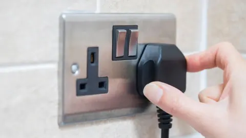  Stock shot of a hand putting a black plug in a stainless steel domestic electricity socket. 