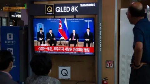 EPA People at a train station in Seoul watch a news report showing Kim and Putin meeting