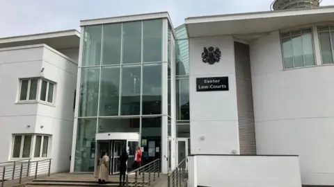 The outside of Exeter Crown Court a white building with a glass front and a royal crest above the words Exeter Law Courts