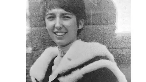 A black-and-white portrait of a person wearing an academic gown with a fur-trimmed hood. The attire suggests a formal graduation or ceremonial occasion. The background appears textured, possibly a stone wall.