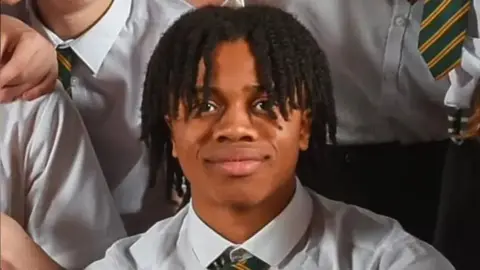 David Ejimofor smiling in a class photo at school. You can see a green and yellow tie being worn by one of his classmates behind him.