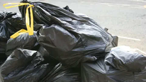 Black bin bags with yellow handles stacked on top of each other 