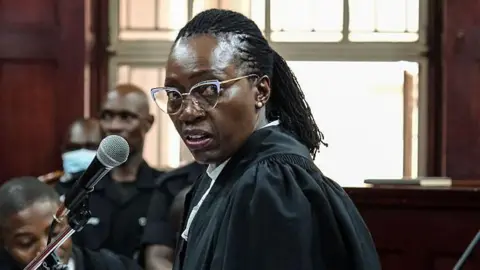 Martha Karua in a black lawyer robe and glasses makes her submission during a court session in Kampala