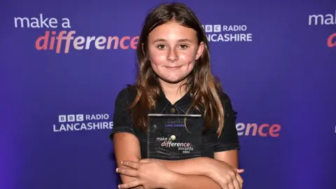 Evie smiling and hugging her square glass  make a difference award