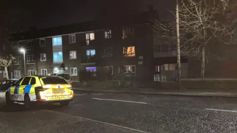 The picture shows a police car parked outside a block of flats on a Belfast Street at night-time