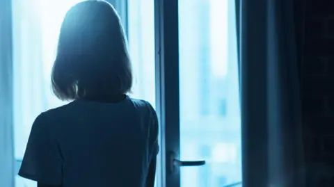 A silhouette of a woman looking through a window