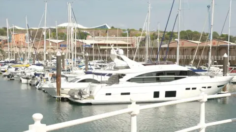 Yachts at the St Helier harbour, with Fort Regent in the background and white iron railings in the foreground.