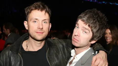 Damon Albarn wearing a black leather jacket with his arm around Noel Gallagher at the Brit Awards 2013