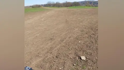 West Yorkshire Police An expanse of open ground that appears heavily worn and damaged. The surface is mostly bare, compacted soil, with little grass remaining.
