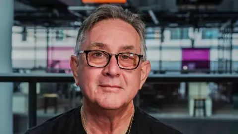 Mick Antoniw wearing glasses and a black t-shirt pictured at BBC Wales' Cardiff headquarters