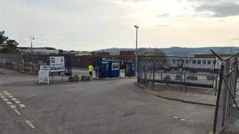 Google Two Royal Navy personnel stand guard at the main entrance to HMS Raleigh in Torpoint. There is a large sign with HMS Raleigh written on it and the gates and security huts at the entrance are navy blue.