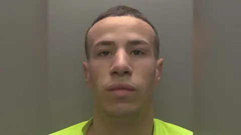 A police handout of a custody photo of Abderrahim Elmuoden, he has short cropped hair and is wearing a fluorescent green T-shirt. 