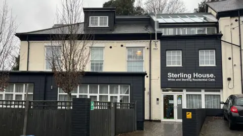 The outside of Sterling House in Norwich. The building is painted cream with some sections including the room painted black. There is a sign on the building which says Sterling House, on it. 