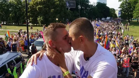 Two men kissing in front of a crowd