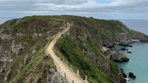 Sark's Coupee bridge - A winding bridge with green cliffs on either side. 