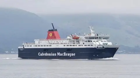 Christopher Brindle The MV Caledonian Isles is a ship with a black lower section with the words Caledonian MacBrayne printed in white along the side of the ship. In smaller white text near the front reads the words Caledonian Isles. The ship is white from the deck up. It sails along the water on a cloudy day. 