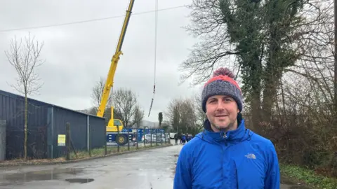 BBC Farmer Dyfan Walters standing in front of a large yellow crane