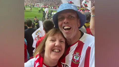 Richard Shelley Richard Shelley (right) and Miranda Shelley (left) they are hugging in the crowd of a Southampton game, celebrating and wearing their Saints tops.