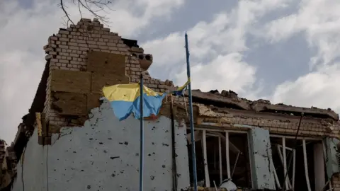 Reuters The Ukrainian flag flies outside the town administration building that was damaged during heavy shelling in the town of Derhachi outside Kharkiv, as Russia"s attack on Ukraine continues, in Ukraine, April 6