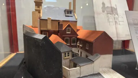 Jo Burn / BBC A miniature model of a number of buildings. It sits in a glass cabinet.