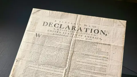 A copy of the US Declaration of Independence. The word "declaration" can be seen in capital letters on the document, which has various folds and creases.