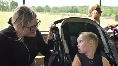 A woman looks lovingly at her baby son. He is in a push chair. 