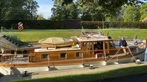 A wooden boat with a man sitting on the front deck.