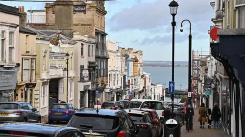 A street scene looking down a hill towards the Solent. There are two and three storey buildings on each side with 