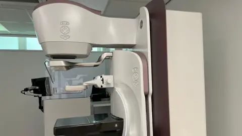 BBC A mammography machine within a Jersey Hospital. It is white black and grey in colour.