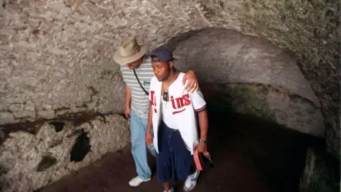 Star Tribune via Getty Images A man has his left arm around the shoulders of another as he consoles him. they are both in a dungeon and walking.