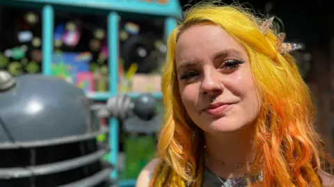Young woman with yellow hair in front of a bright shop front