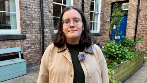 DAVE EDWARDS/BBC A woman looks at the camera. She has dark hair, glasses and a neutral expression