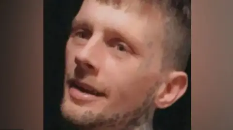 Pictured is Kyle Pugh. He has blonde hair and face tattoos along his jaws line and at the side of his temple.