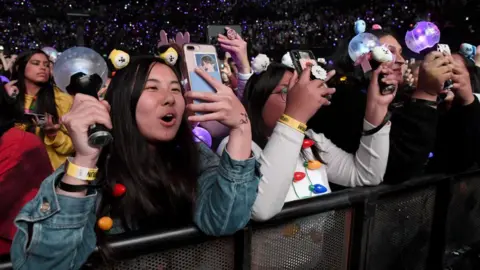FilmMagic via Getty Images Fans holding their phones up behind a barricade at a concert