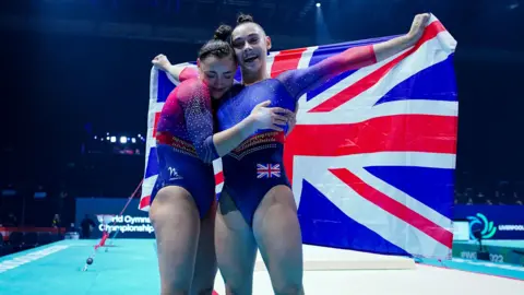 PA Media The Gadirova twins are dressed in red and blue leotards and holding the union flag behind them at the World Gymnastics Championship.