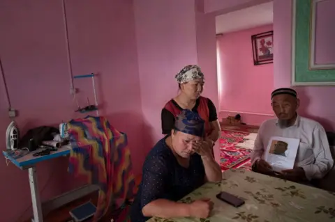 Getty Gulnar Kosdaulet, 46, Gulzira Auelkhan, 40, Akbar Yenkelesh, 77, in their home in the village of Akshi near (100miles+) the border with China. Kosdaulets husband is still being held in a camp in Xinjiang. Auelkhan was detained in the camps in Xinjiang for 18 months. Yenkelesh, the father of Kosdaulets husband, holds up a photo of his son, Sarsenbek Akbar, 45.