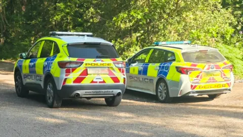 Two police cars are parked near trees